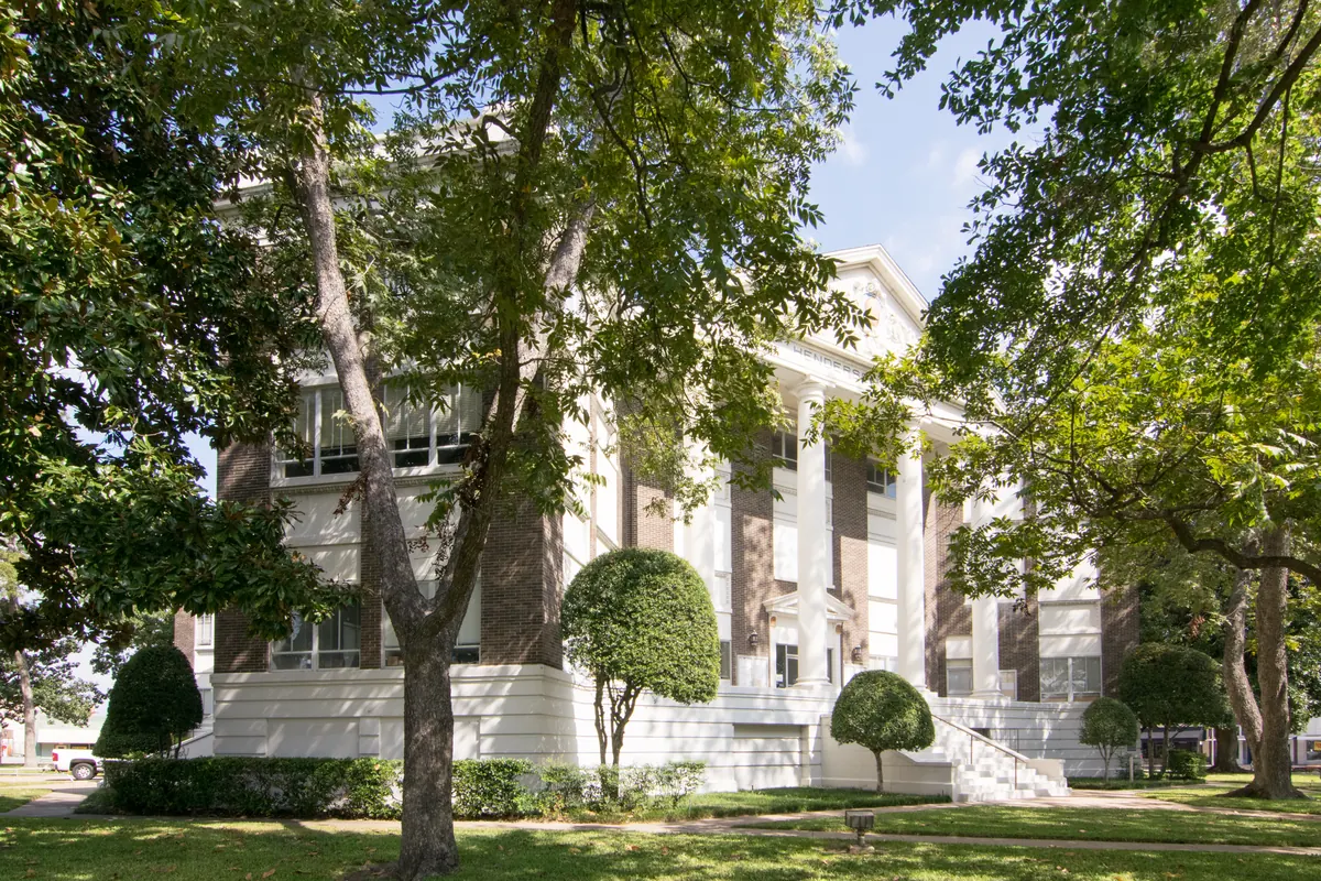 The Henderson County Courthouse in Athens, a white building with tall columns, framed by shade trees and trimmed shrubs.