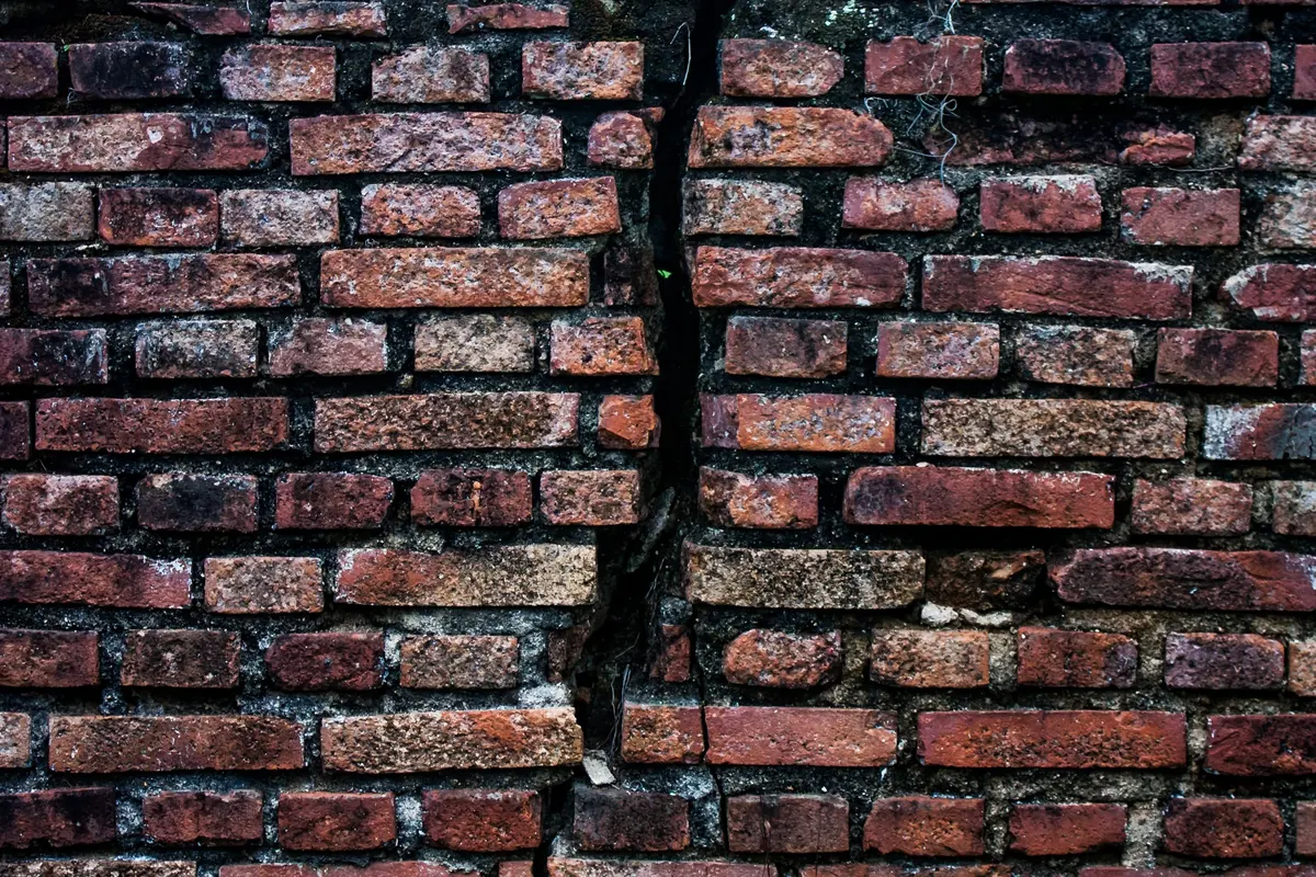A long crack running down through the bricks and mortar of an old red brick wall.
