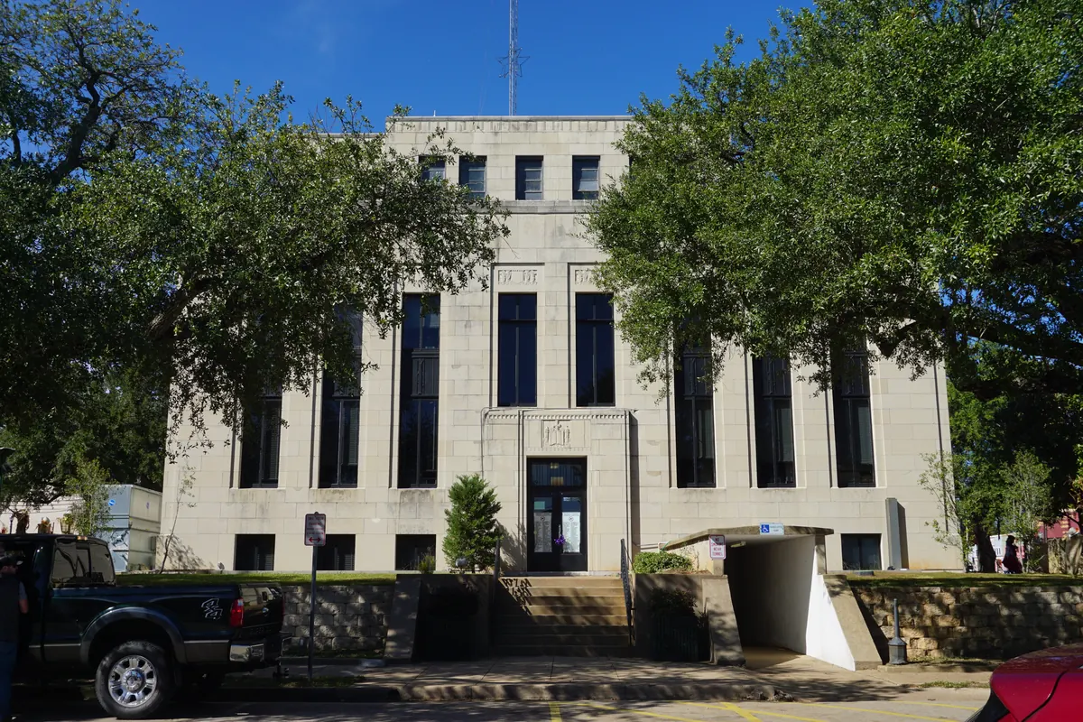 The Van Zandt County Courthouse in Canton, a pale stone building with tall narrow windows, between shade trees.