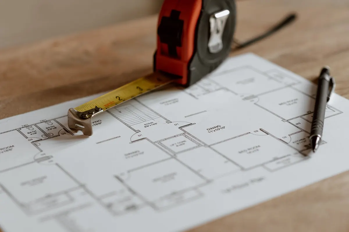 A tape measure and a pen resting on a printed floor plan of a house.