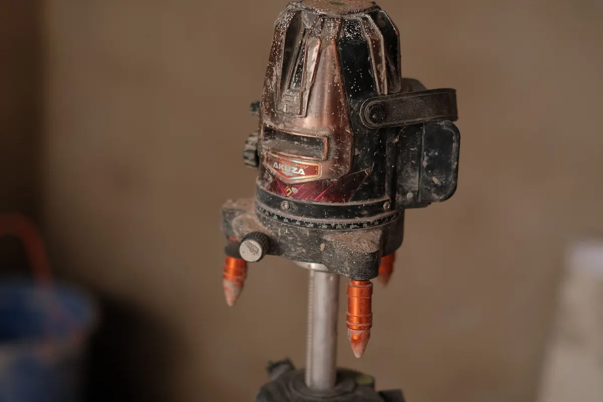 A dusty laser level mounted on a tripod inside a building.