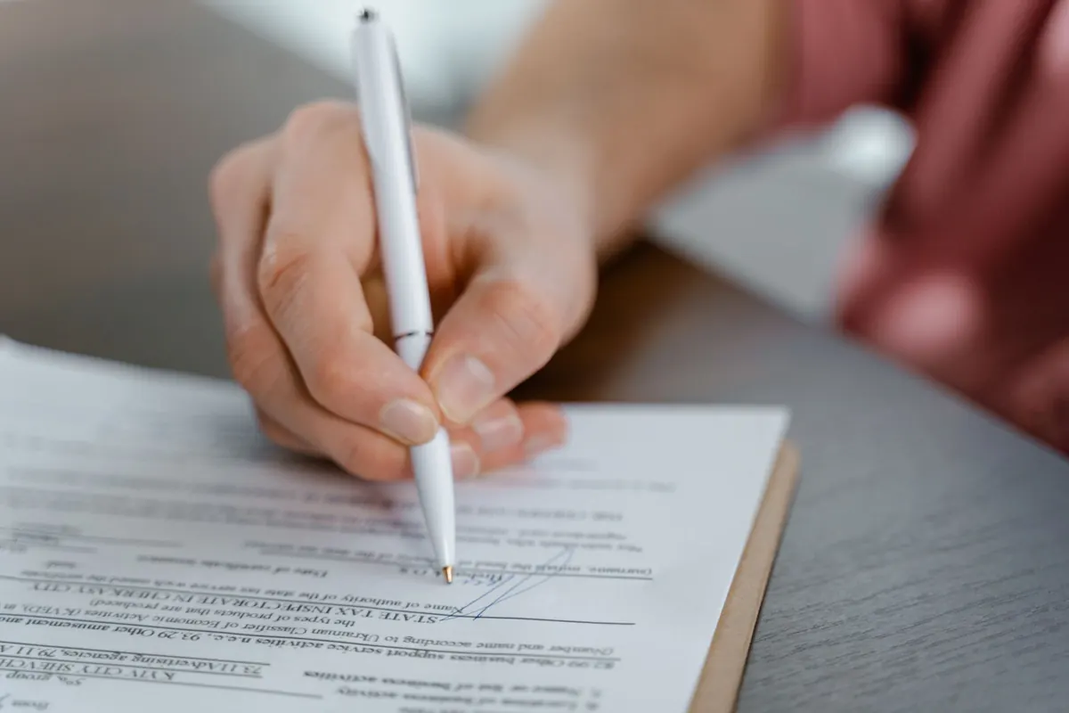 A hand holding a pen over a printed agreement on a clipboard.
