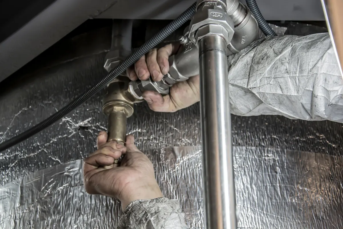A plumber's hands tightening a brass fitting on a metal water pipe.