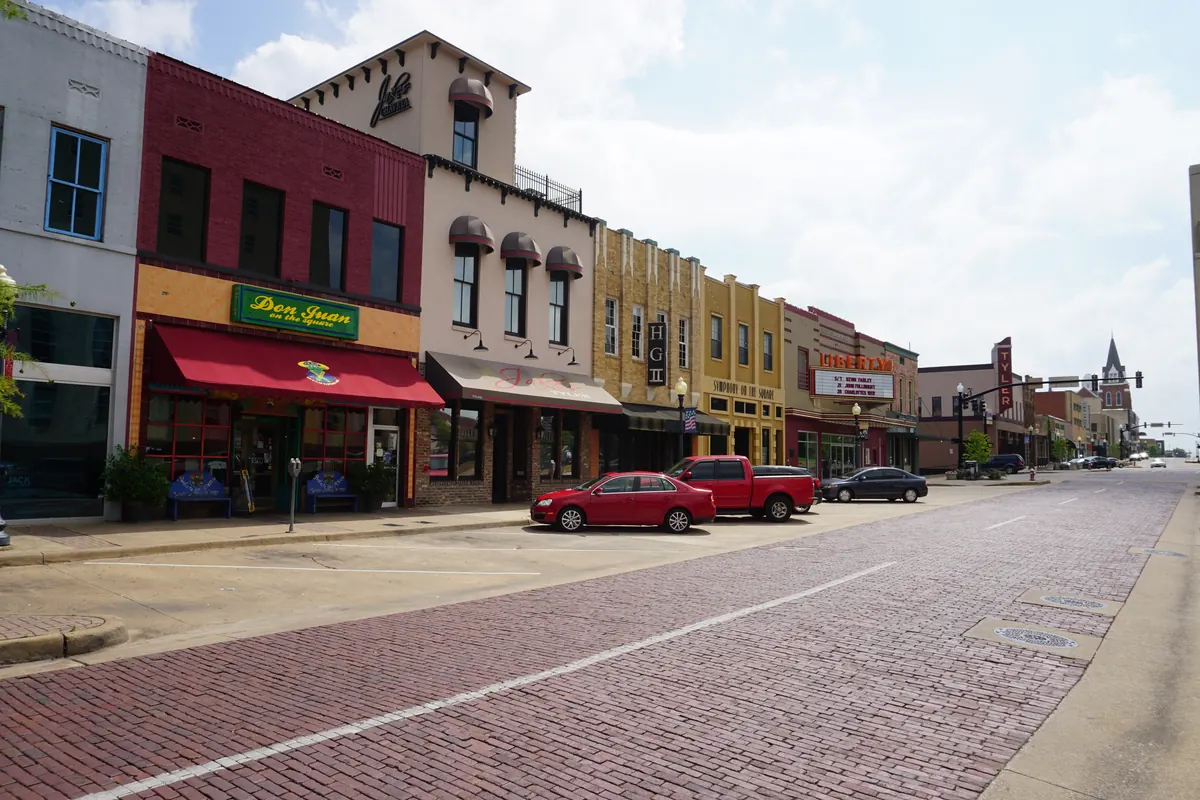 A brick-paved street in downtown Tyler lined with two-story brick storefronts and parked cars.